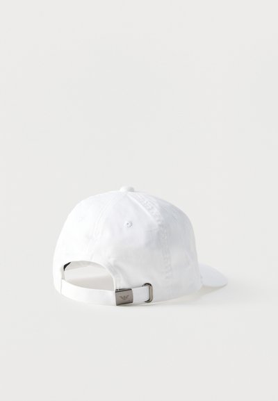 Valge pesapallimüts, nähtud tagantpoolt, reguleeritava rihmaga, millel on väike metallist klamber, ühtlasel taustal.