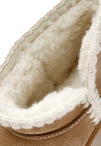 Tan suède boot met een zachte witte fleece voering, voorzien van decoratieve stiksels en een textuur naad rond de opening.