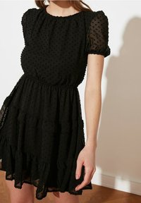 Vestido negro de manga abullonada hecho de un tejido texturizado con lunares, que presenta un dobladillo con volantes y una cinturilla elástica para una silueta ajustada.