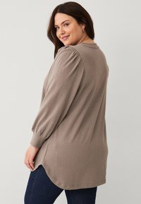 Taupe long-sleeve top with puffed sleeves, rounded hem, and soft cotton fabric. Features a relaxed fit and side slits for ease of movement.