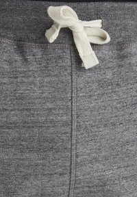 Pantalones de chándal grises con una tela texturizada, que presentan un cordón en color blanco roto y costuras visibles a lo largo de la cinturilla y las costuras.