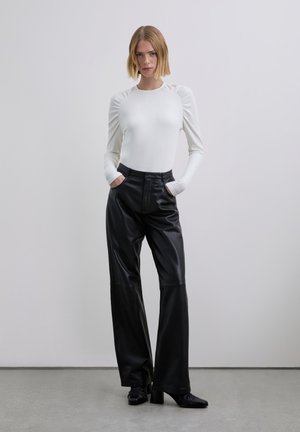 Haut blanc à manches longues côtelées avec détails froncés aux épaules, associé à un pantalon en cuir noir taille haute et des chaussures noires à talons.