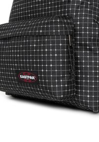 Mochila Eastpak en negro y gris con un patrón de cuadrícula, material resistente, bolsillo exterior con cremallera y un parche de logo rojo.