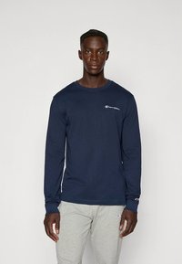 Marineblauw T-shirt met lange mouwen van een katoenmengsel, met een klein geborduurd logo op de borst en geribbelde boordjes, gecombineerd met grijze sweatpants.