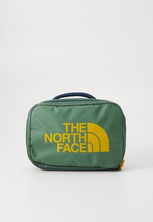 Saco de tecido verde com um padrão em grelha, apresentando um logo amarelo "THE NORTH FACE" e um detalhe de design curvo. Inclui uma alça azul.