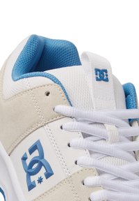 Białe i jasnoszare buty do jazdy na deskorolce z niebieskimi akcentami, z teksturowaną zamszową cholewką, sznurowanym zapięciem oraz wyraźnym logo DC z boku.