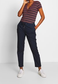 Pasek, krótkorękawowy top w kolorze granatowym w czerwono-białe paski; granatowe spodnie z troczkiem; białe sneakersy; codzienny fason, luźny styl.