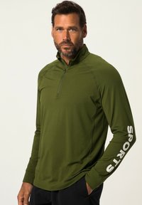 Maglietta a maniche lunghe verde oliva con colletto a zip quarti, caratterizzata da testo grigio chiaro "SPORTS" sulla manica sinistra e una superficie liscia e elastica.