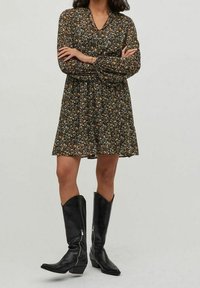 Svart blommönstrad klänning med långa ärmar, V-ringning, rynkad midja och knälång nederkant; matchad med knähöga svarta läderstövlar.