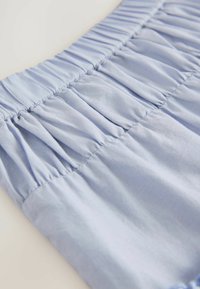 Tissu bleu clair avec une texture froncée, présentant un design smocké à la taille et une finition lisse. Matériau doux et léger.