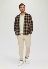 Zwart en beige geruite flanellen shirt over een lichtgroen V-hals t-shirt, gecombineerd met beige corduroy broek en witte sneakers.