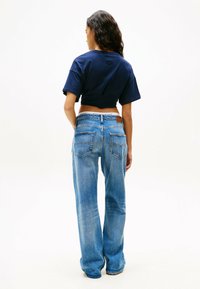 Marineblauw cropped t-shirt gecombineerd met lichtblauwe wijde jeans. De jeans hebben twee achterzakken en een bruine leren taillebanddetail.