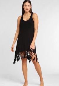 Vestido negro sin mangas con un corte holgado, que presenta un dobladillo con flecos y largas hebras anudadas. Fabricado en una tela suave y ligera.