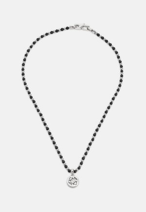 Collier en argent avec de petites perles noires et un pendentif rond en argent présentant un design entrelacé élégant, sur un fond uni.