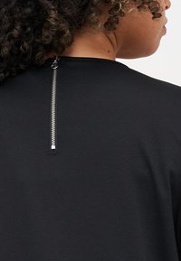 Black textile top featuring a metallic zipper detail at the back neckline, with a smooth texture and classic crew neck design.