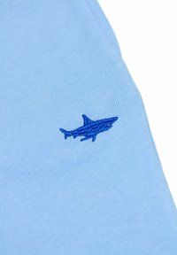Jasnoniebieska bawełniana koszula z niebieskim haftowanym wzorem rekina. Materiał ma gładką teksturę i dopasowany krój.
