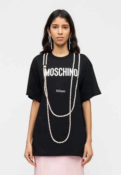 T-shirt noir oversize avec inscription blanche "MOSCHINO Milano", orné de chaînes de perles roses. Tissu lisse, manches courtes, coupe décontractée.