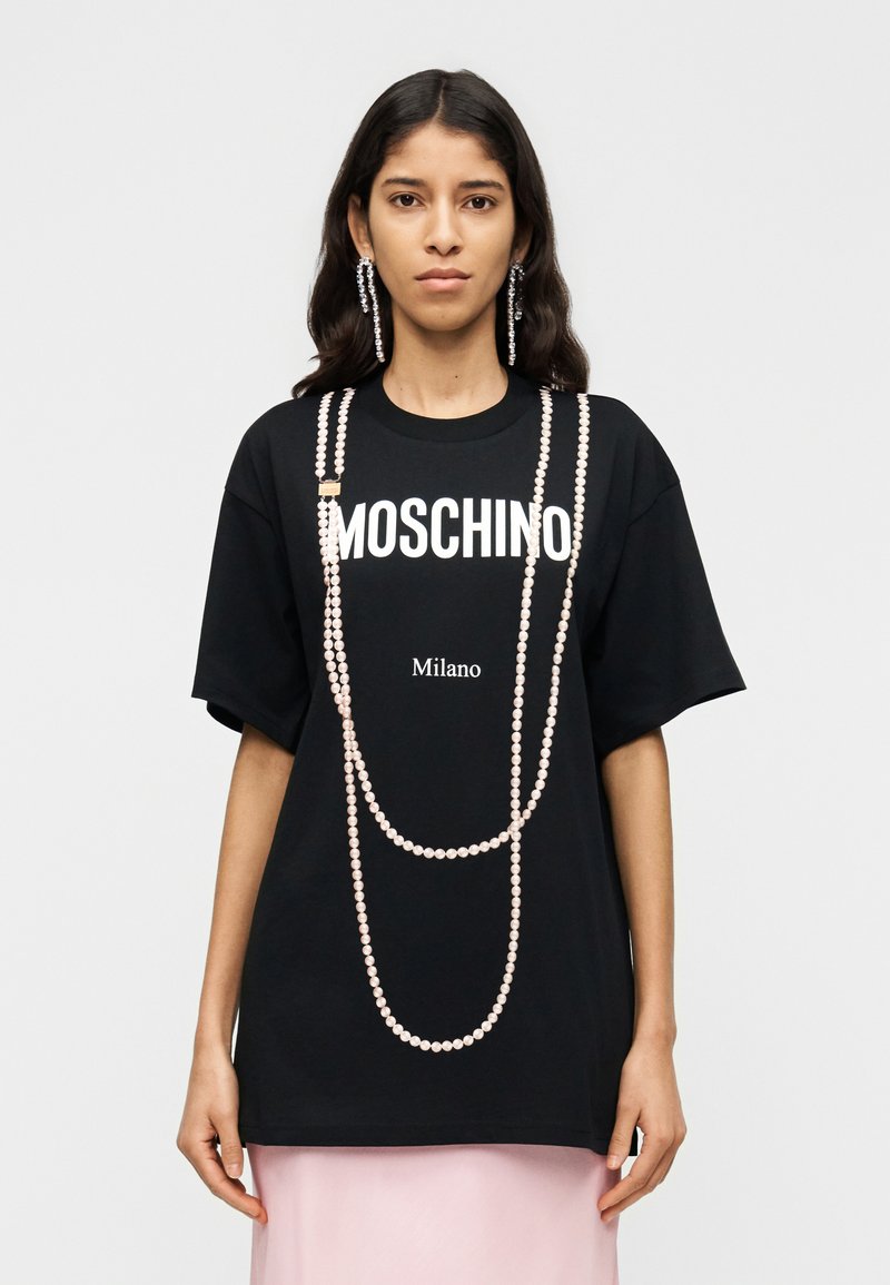 Μαύρο φαρδύ t-shirt με λευκή εκτύπωση "MOSCHINO Milano", διακοσμημένο με ροζ καλοσχηματισμένες αλυσίδες από χάντρες. Λείο ύφασμα, κοντά μανίκια, άνετη γραμμή.