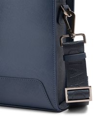 Navyblaue synthetische Tasche mit strukturiertem Oberflächen, glatten Akzenten, einem abnehmbaren Tragegurt mit gemustertem Detail und einem metallischen Verschluss.
