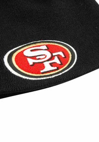 Schwarz gestrickte Mütze mit einem gestickten ovalen Logo in rot, weiß und schwarz, das "SF" in fetter Schrift zeigt.