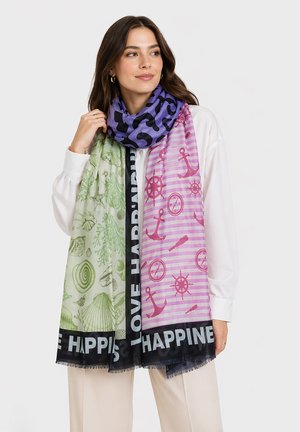 Frau trägt bunten Schal mit grünem Meeresleben, lila Tierprint und pinken nautischen Mustern über weißer Bluse und beiger Hose.