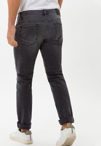 Dark grey denim jeans with a slim fit, rolled cuffs, and two back pockets. Paired with white sneakers featuring a light grey accent.