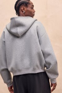 Sweat à capuche gris, coupe oversize, texture douce, bord-côtes à l'ourlet et aux poignets, avec une vue arrière simple sur un fond neutre.