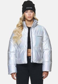 Irideszente silberne Pufferjacke mit hohem Kragen und Reißverschluss vorne. Kombiniert mit einer schwarzen Mütze, die weißen Text zeigt.