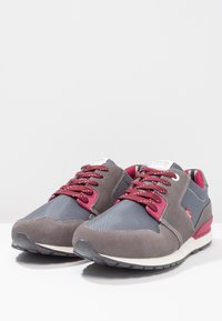 Graue und marineblaue Sneakers mit einem Obermaterial aus Wildleder und Mesh, ausgestattet mit kastanienbraunen Schnürsenkeln, strukturierten Akzenten und einer weißen Sohle.