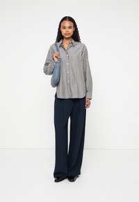 Camicia a righe grigia e bianca, abbinata a pantaloni a gamba larga blu navy e una piccola borsa a tracolla blu. Tessuti morbidi, vestibilità rilassata.
