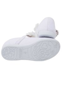 Scarpa slip-on in tessuto bianco con suola testurizzata che presenta motivi floreali e a cuore. Il design include un piccolo accento decorativo a forma di fiore.