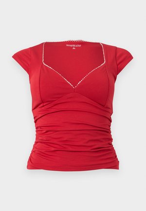 Κόκκινο εφαρμοστό τοπ με κοντά μανίκια και τετράγωνο ντεκολτέ, με λεπτή λευκή διακοσμητική φάσα με κυματιστές άκρες και λεπτομέρειες ζώνης με πιέτες στη μέση.