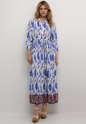 Maxikleid mit weißem Grund, blauem Blumenmuster und braunem Saum. Verfügt über einen kragenförmigen Ausschnitt, eine taillierte Taille und dreiviertellange Ärmel.