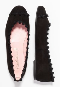 Ballerines en suede noir avec un bout arrondi et un bord orné de pompons, dotées d'une semelle intérieure rose pâle et d'une semelle noire plate.