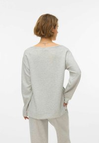 Svijetlosiva majica dugih rukava s širokim izrezom, spuštenim ramenima i opuštenim krojem, izrađena od meke tkanine glatke teksture.