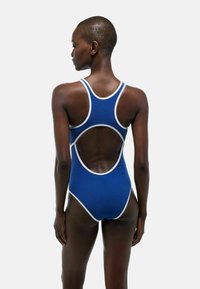 Maillot de bain une pièce bleu avec des accents blancs, doté d'un design dos nageur et d'une ouverture à mi-dos pour faciliter le mouvement et la ventilation.