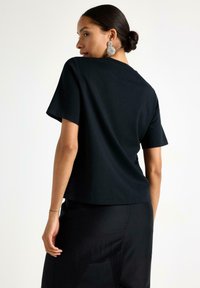 Sort t-shirt med korte ærmer og en afslappet pasform, der har en blød tekstur og en rund halsudskæring, kombineret med sorte bukser.