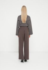 Striped long-sleeve top in brown and white, paired with high-waisted brown wide-leg trousers and black heeled shoes. Visible back details include seams.