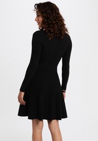 Schwarzes geripptes Kleid mit langen Ärmeln, tailliertem Oberteil und ausgestelltem, plissiertem Rock. Strukturierter Stoff und elastischer Bund für zusätzlichen Komfort.