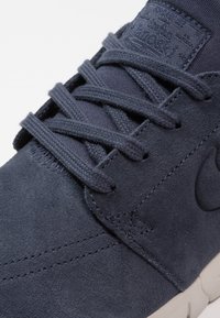 Mörkblå mockasneakers med platta snören, vadderad tunga och subtil branding. Gummisula med ljusgrå accenter och ton-i-ton sömnadsdetaljer.