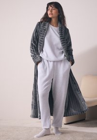 Grijze gestreepte pluche badjas gecombineerd met een lichtgrijze geribbelde top en bijpassende broek. Zacht textiel met een ontspannen pasvorm en zijzakken.