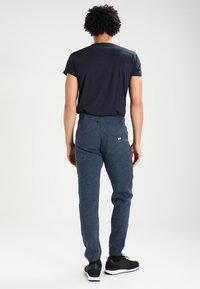Navyblauwe joggers van gestructureerde stof, met een achterzak met een logo patch en elastische boorden, gecombineerd met een donker t-shirt.