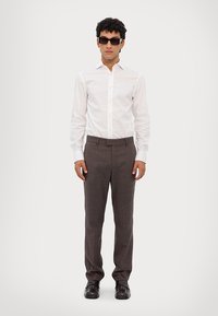 White button-up shirt with a pointed collar, paired with brown pinstriped trousers. Black leather shoes and sunglasses complete the outfit.