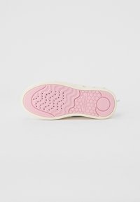 Hvit sneakers med en teksturert gummi yttersåle som har et rosa bølgete mønster og sirkulære detaljer. Logo synlig på sålen.