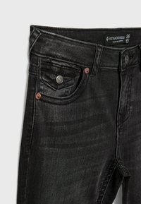 Jeans de mezclilla negra con un ajuste slim, que cuentan con un diseño clásico de cinco bolsillos, remaches de cobre y una pequeña etiqueta de la marca en la cinturilla.
