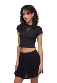 Top corto nero a coste con un ricamo a forma di farfalla sul petto; abbinato a una mini gonna nera a strati con ruches.