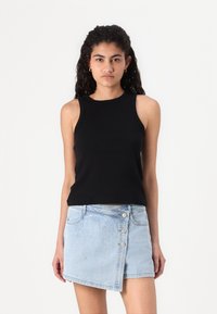 Black sleeveless ribbed top paired with a light blue denim miniskirt, featuring silver studs and a diagonal button closure.