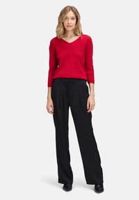 Roter gestrickter Pullover mit V-Ausschnitt und Dreiviertelärmeln, kombiniert mit schwarzen weiten Hosen und schwarzen High Heels.