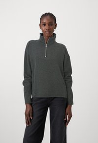 Felpa zipata verde scuro con colletto alto, realizzata in materiale morbido, caratterizzata da maniche lunghe e una vestibilità rilassata.