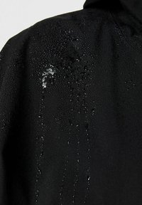 Veste imperméable noire avec des gouttes d'eau perlant sur le tissu, affichant une texture lisse et des caractéristiques de design minimales.